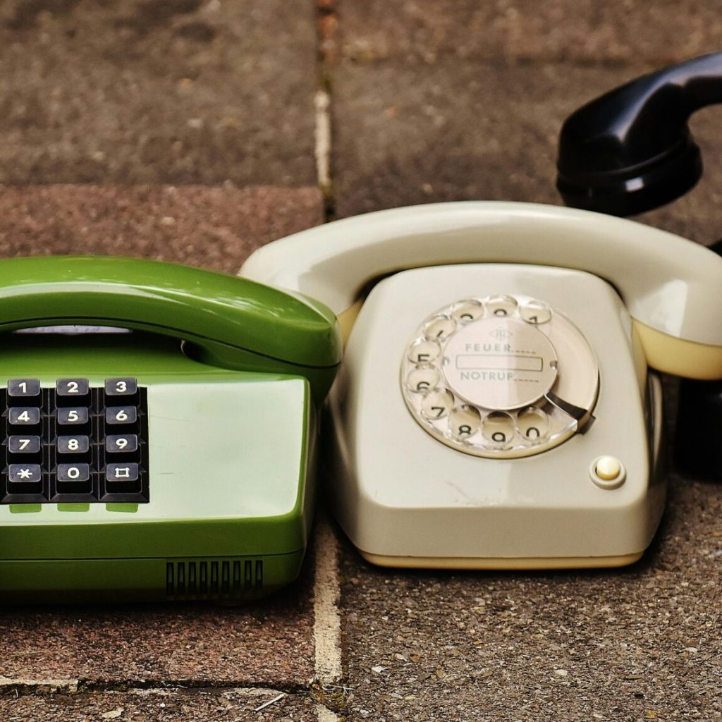 A variety of antique, vintage, and modern telephones displayed on pavement.